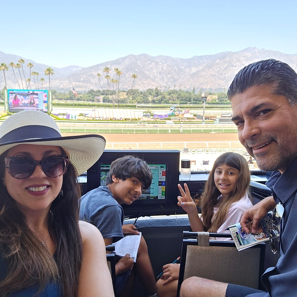 The Leaven Life family smiling together in their seats at the racetrack, with palm trees and mountains behind them
